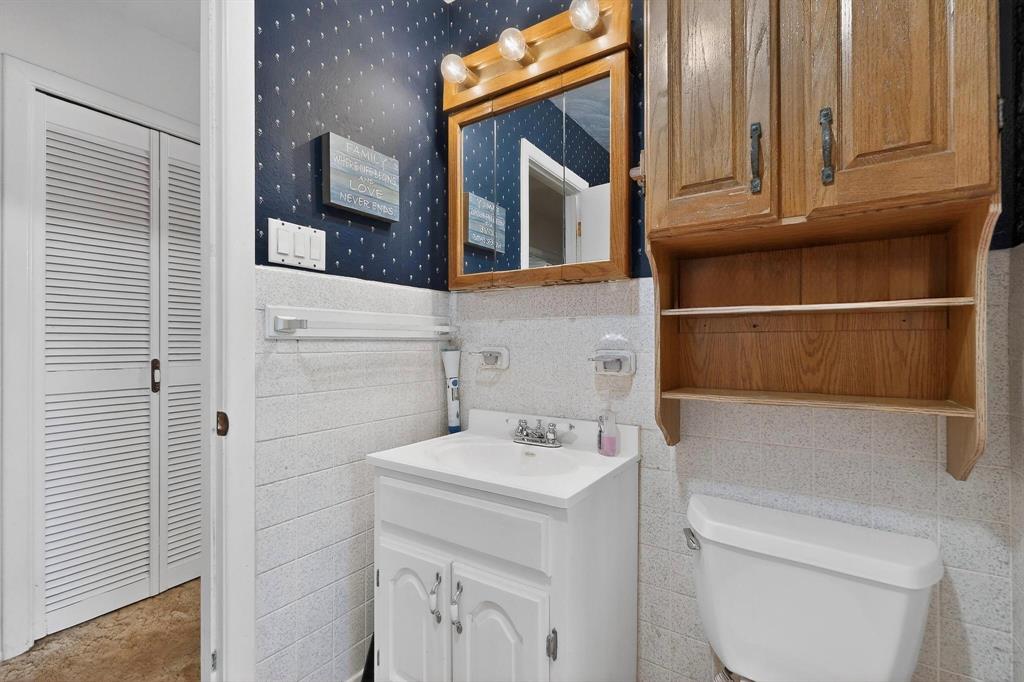 202 Senter Valley Road Irving, TX 75060 - Photo 22 of 32 Bathroom featuring a white vanity with a ceramic sink, a wooden medicine cabinet, a wooden wall-mounted storage cabinet with open shelving, and white louvered bifold doors