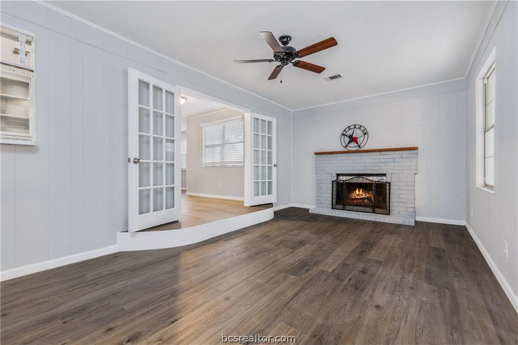 3755 West Villa Maria Road Bryan, TX 77807 - Photo 7 of 26 Unfurnished living room with crown molding, dark wood finished floors, a fireplace, ceiling fan, and french doors