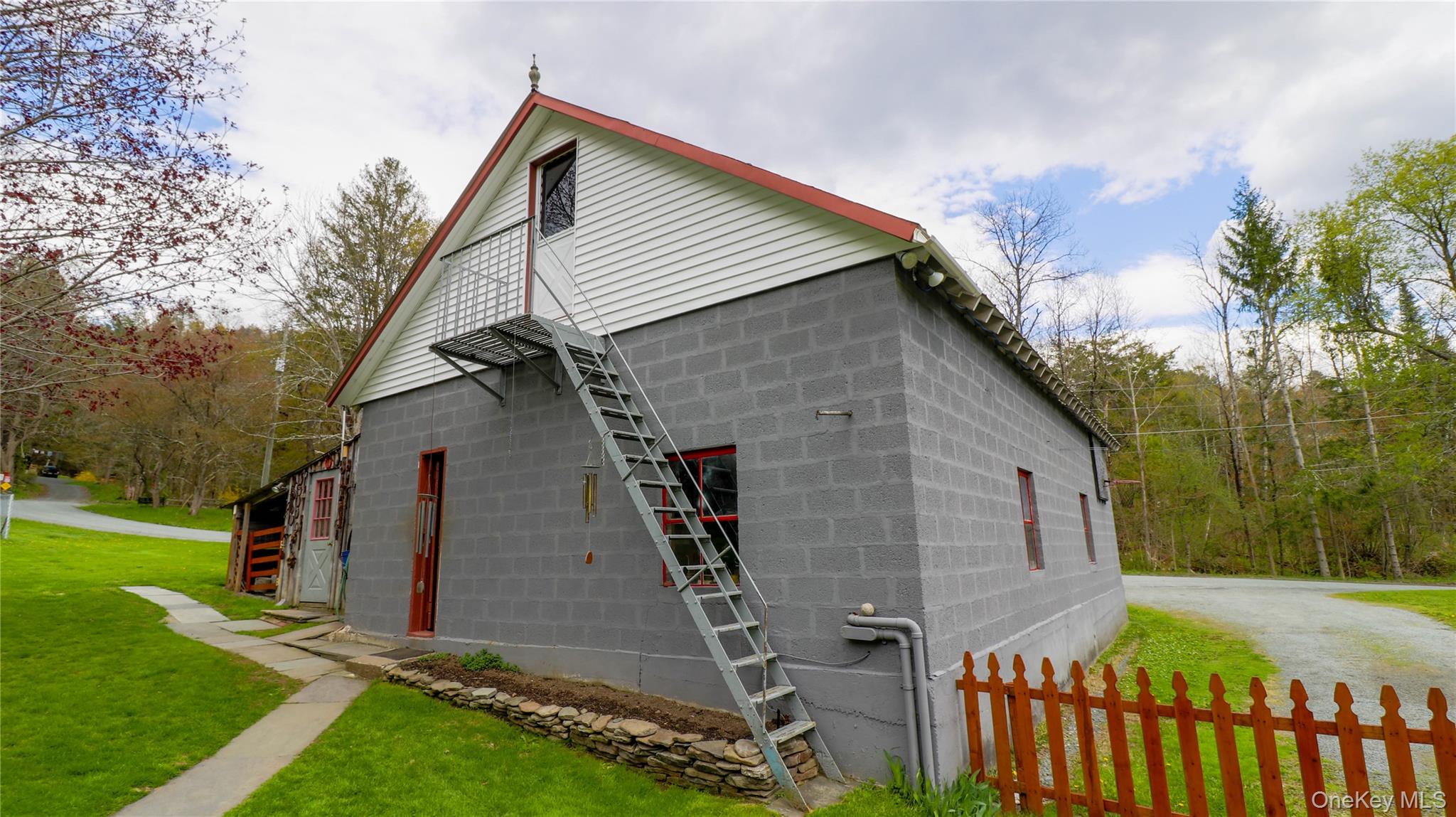 11 Hood Road Roscoe, NY 12776 - Photo 24 of 31 Gray cinder block exterior with a white gable-end facade, red-trimmed roofline, and an external metal staircase leading to a second-story balcony