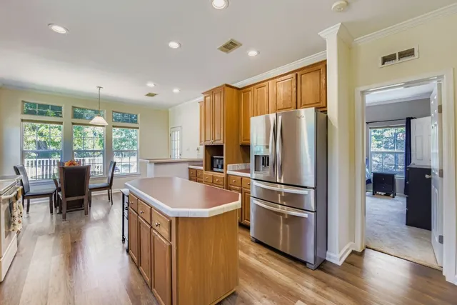 a kitchen with stainless steel appliances granite countertop a refrigerator a stove a sink a dining table and chairs with wooden floor