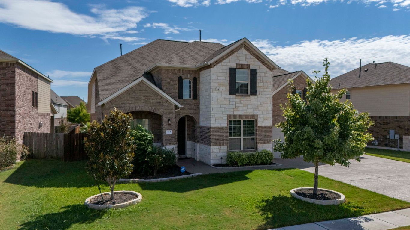 French country home with stone siding, brick siding, driveway, and roof with shingles