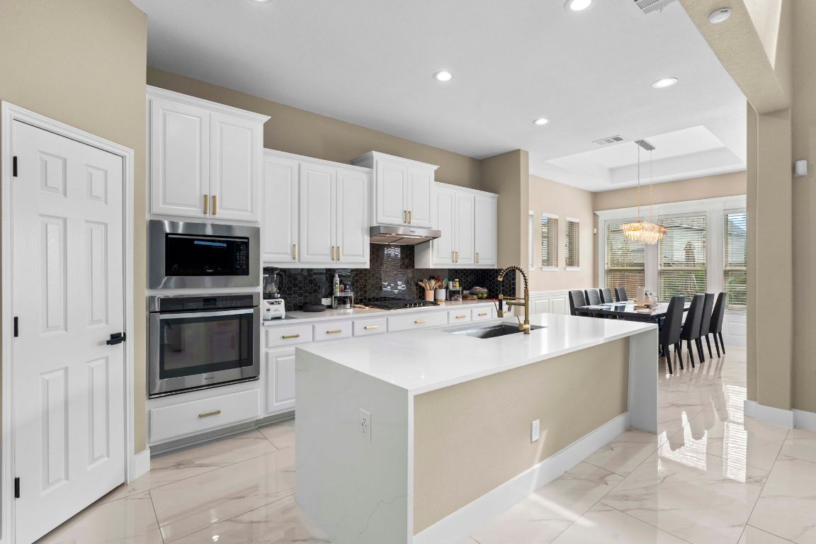 3301 Falconers Way Pflugerville, TX 78660 - Photo 19 of 39 Kitchen featuring hanging light fixtures, backsplash, appliances with stainless steel finishes, a tray ceiling, and a center island with sink