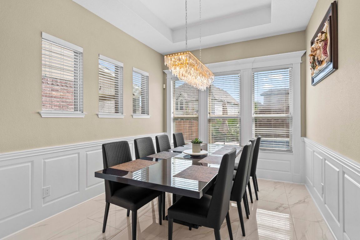 3301 Falconers Way Pflugerville, TX 78660 - Photo 21 of 39 Dining area with a decorative wall, a wainscoted wall, a chandelier, a tray ceiling, and light marble finish floors