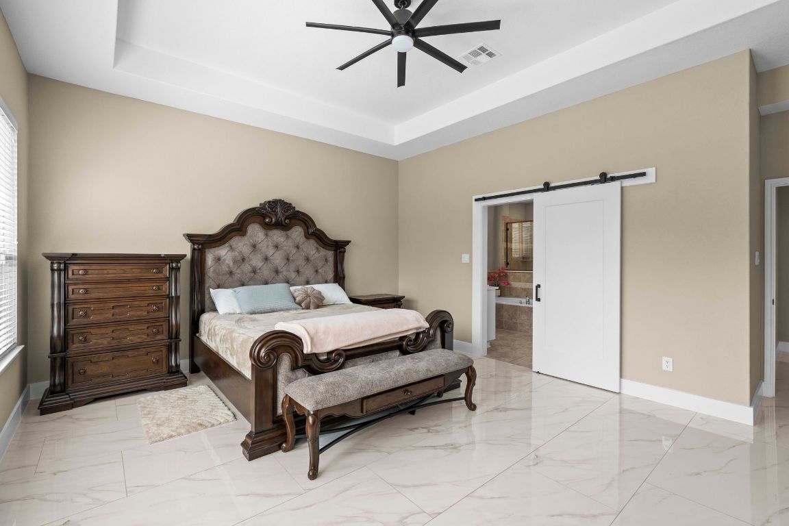 3301 Falconers Way Pflugerville, TX 78660 - Photo 24 of 39 Bedroom featuring a barn door, a raised ceiling, light marble finish floors, and a ceiling fan
