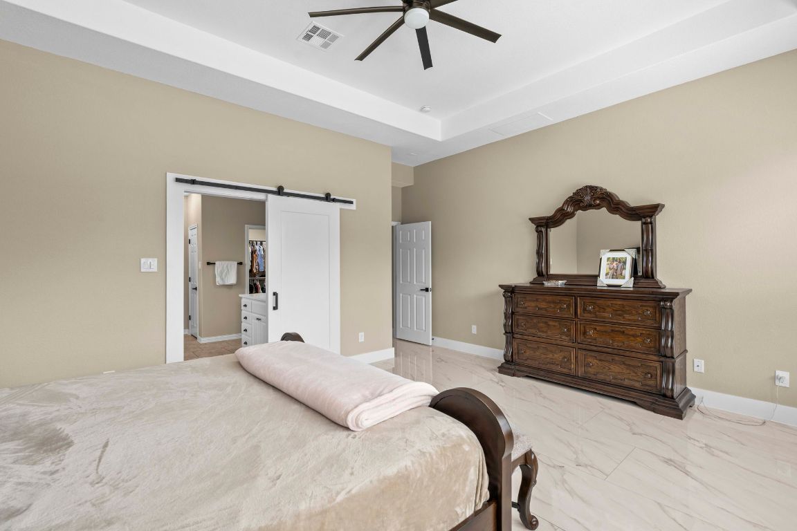 3301 Falconers Way Pflugerville, TX 78660 - Photo 25 of 39 Bedroom with a barn door, a ceiling fan, a spacious closet, light marble finish flooring, and a raised ceiling