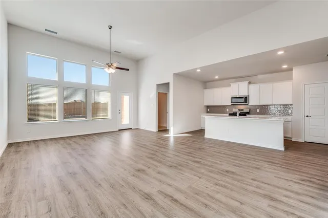 a view of an empty room with wooden floor and a kitchen
