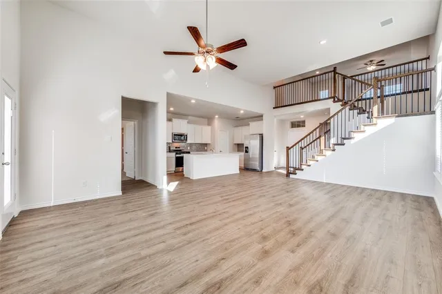 a view of an empty room with wooden floor and a ceiling fan