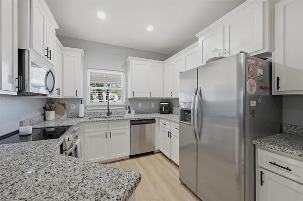 a kitchen with stainless steel appliances granite countertop a refrigerator a sink a stove and white cabinets