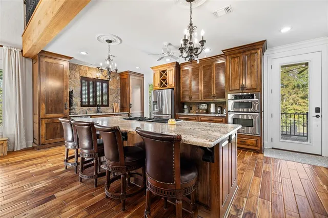 a open kitchen with stainless steel appliances granite countertop a refrigerator a stove top oven a dining table and chairs with wooden floor