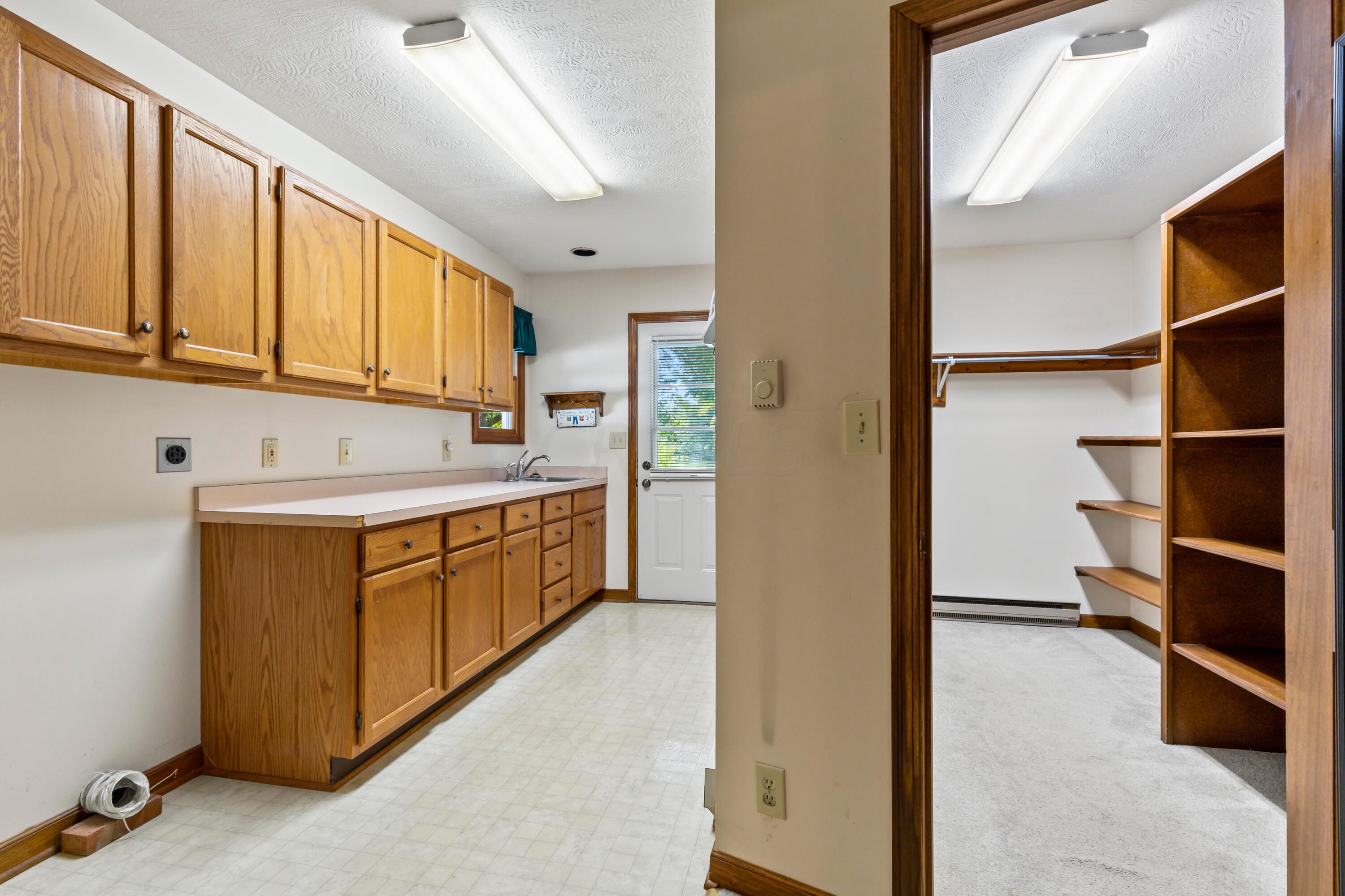 5764 Cheshire Road Galena, OH 43021 - Photo 18 of 59 • Neutral vinyl flooring
• Tan painted walls
• Wall cabinets
• Enclosed & extended vanity
• Single bowl, stainless steel
sink
• Built-in ironing board
• Electric dryer hookup
• Rear service door
• Step-in closet