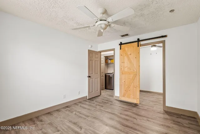 a view of an empty room with wooden floor and a ceiling fan