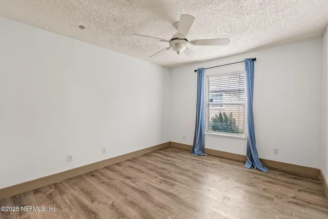 an empty room with wooden floor fan and windows
