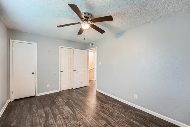 an empty room with wooden floor ceiling fan and windows