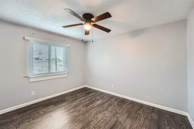 an empty room with wooden floor fan and windows
