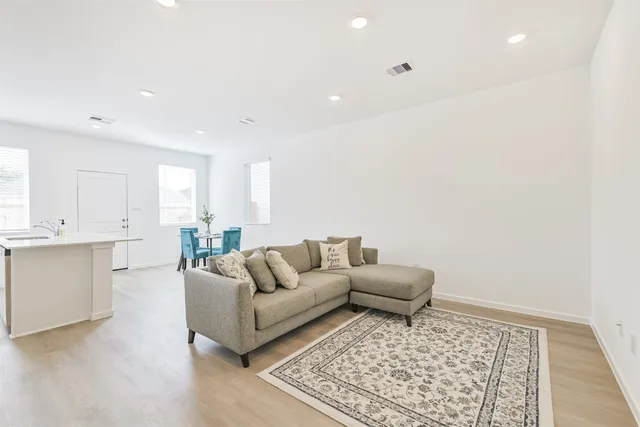 a living room with a couch and white kitchen with wooden floor