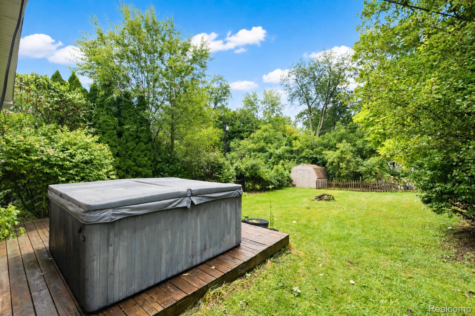 535 Snyder Road Highland, MI 48357 - Photo 4 of 23 Expansive backyard featuring a wood deck with a built-in hot tub, lush green lawn, and mature trees
