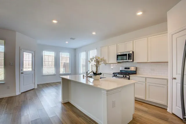 a kitchen with stainless steel appliances a stove a sink a refrigerator white cabinets and wooden floor