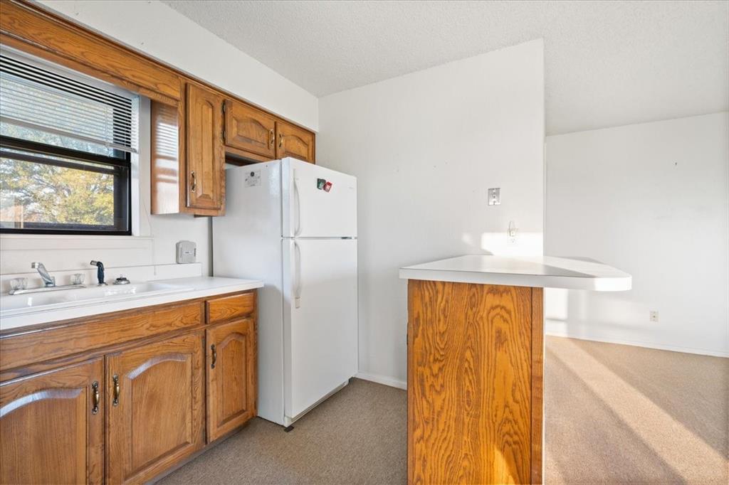 105 Riverside Drive Mineral Wells, TX 76067 - Photo 33 of 40 Kitchen with brown cabinets, light countertops, freestanding refrigerator, and light colored carpet