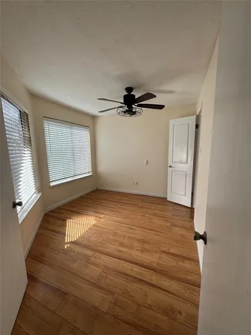 an empty room with wooden floor fan and windows