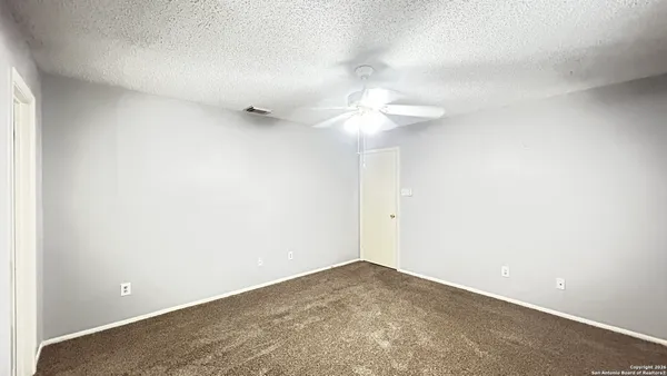 an empty room with a chandelier fan and wooden floor