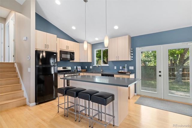 a kitchen with kitchen island granite countertop a refrigerator a stove a sink a dining table and chairs with wooden floor