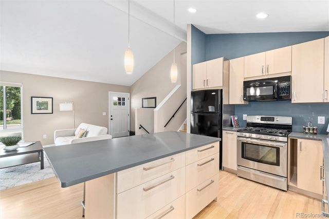a living room with stainless steel appliances kitchen island granite countertop a stove a sink dishwasher and a microwave oven with white cabinets