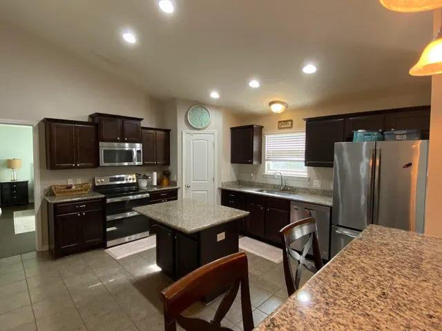 a kitchen with stainless steel appliances granite countertop a refrigerator a stove a sink a dining table and chairs