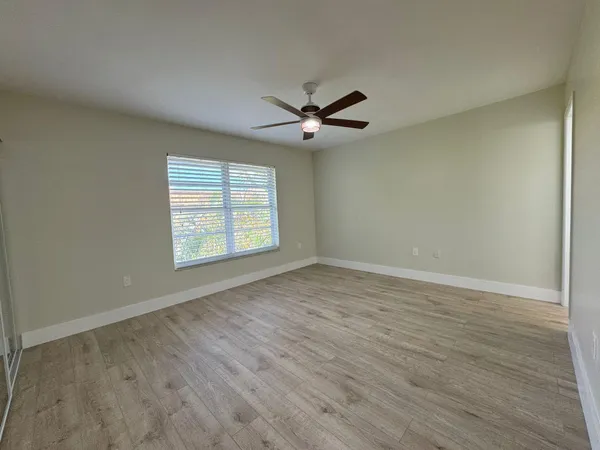 an empty room with wooden floor ceiling fan and windows