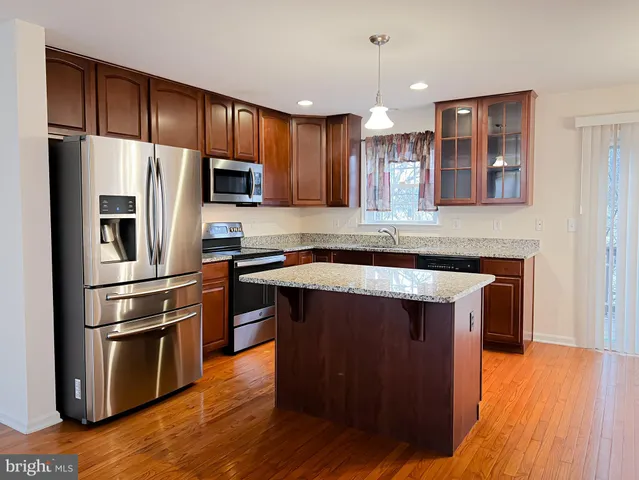 a kitchen with kitchen island wooden floors appliances and cabinets