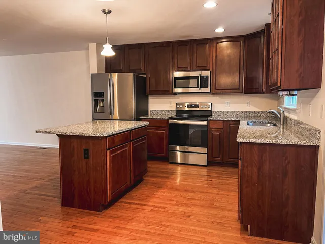 a kitchen with stainless steel appliances granite countertop wooden cabinets a stove top oven a sink and dishwasher with wooden floor