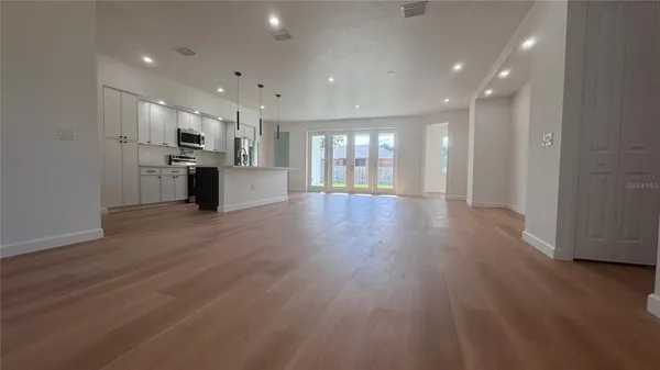a view of an empty room and kitchen with wooden floor