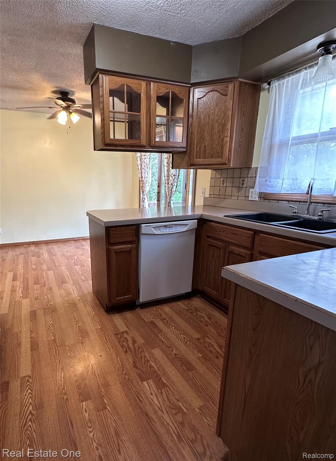 2430 Coolidge Road Barryton, MI 49305 - Photo 18 of 29 Kitchen featuring wood-finish flooring, wood cabinetry with glass-front uppers, a built-in dishwasher, and a double basin sink