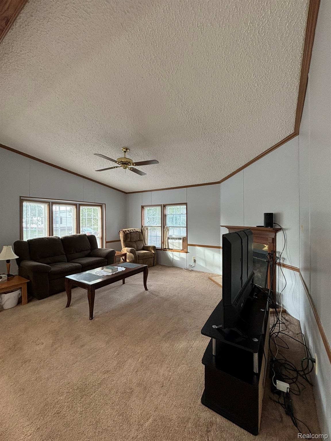 2500 Mann Road Clarkston, MI 48346 - Photo 6 of 28 Carpeted living area featuring ornamental molding, a textured ceiling, a decorative wall, and a ceiling fan