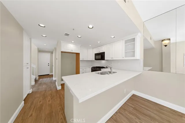 a large white kitchen with a refrigerator a sink dishwasher a stove and white cabinets with wooden floor