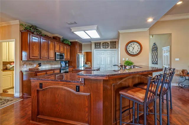 a kitchen with stainless steel appliances granite countertop a stove top oven a refrigerator a dining table and chairs with wooden floor