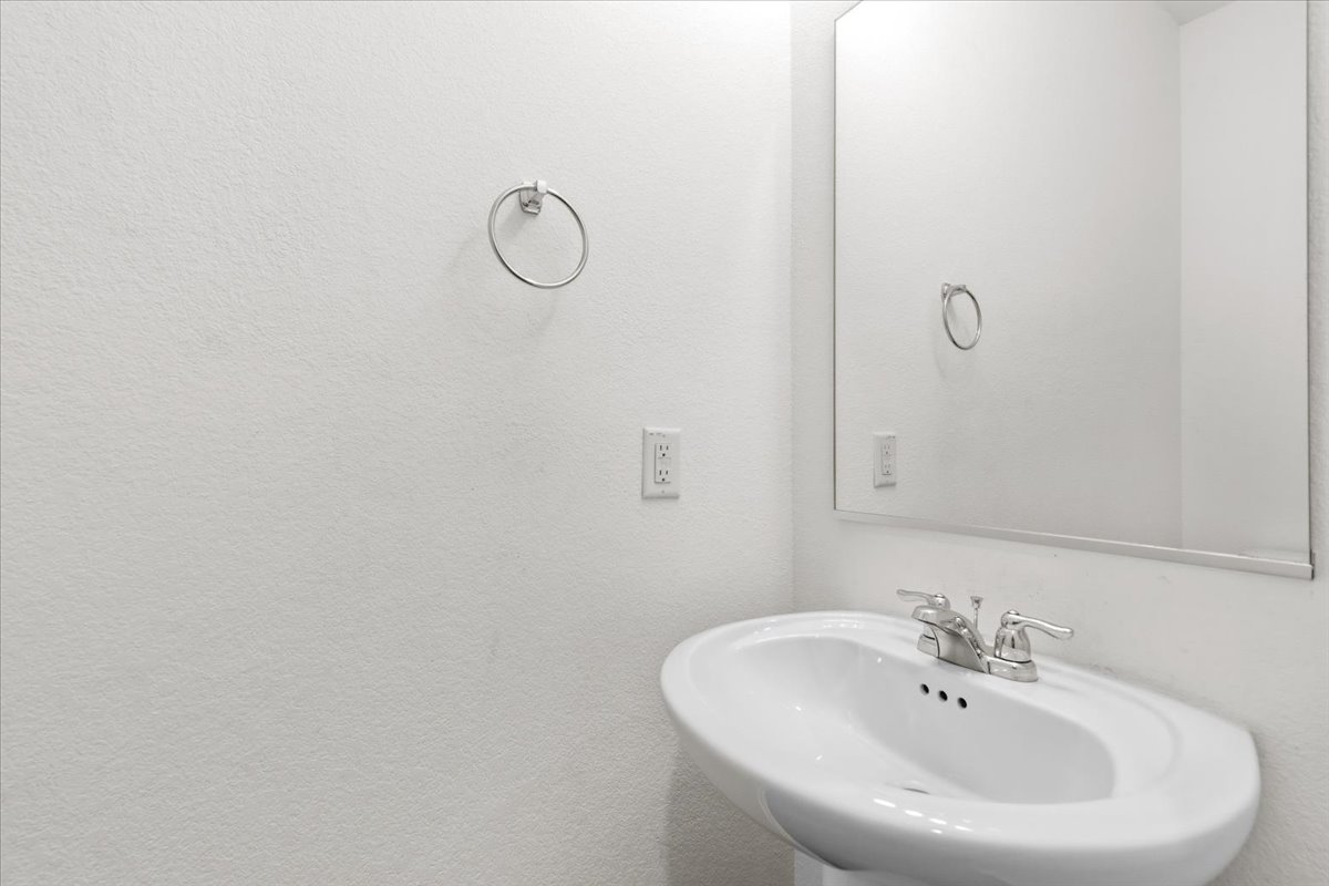 101 Rowdy Yates Way Jarrell, TX 76537 - Photo 27 of 32 Pedestal sink with chrome faucet, large frameless mirror, and a silver-tone towel ring