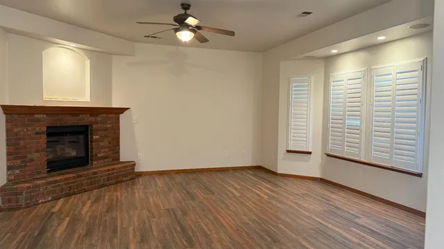 a view of an empty room with wooden floor fireplace and a window