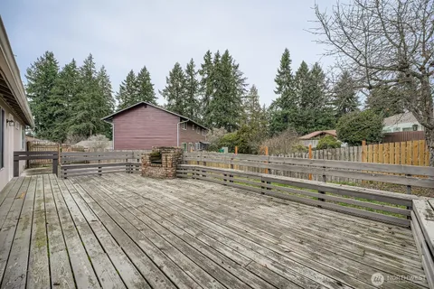 a view of house with deck outdoor seating and trees in the background