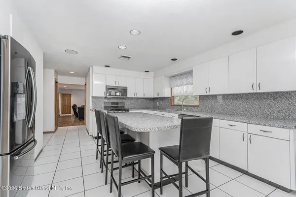 a kitchen with stainless steel appliances granite countertop a stove top oven a refrigerator a sink and white cabinets