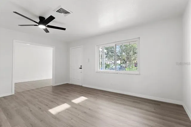 an empty room with wooden floor fan and windows