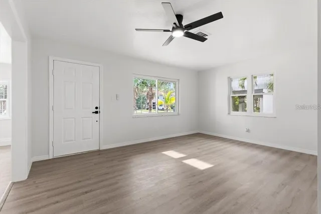 an empty room with wooden floor ceiling fan and windows