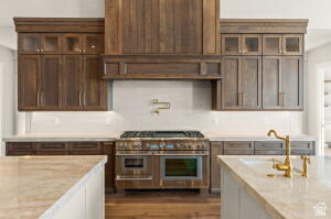 1141 East Lost Ridge Drive Washington, UT 84780 - Photo 37 of 108 Gourmet kitchen featuring a wood-paneled range hood, professional-grade stainless steel range with double ovens, ample wood cabinetry, light-toned countertops, and a white tile backsplash