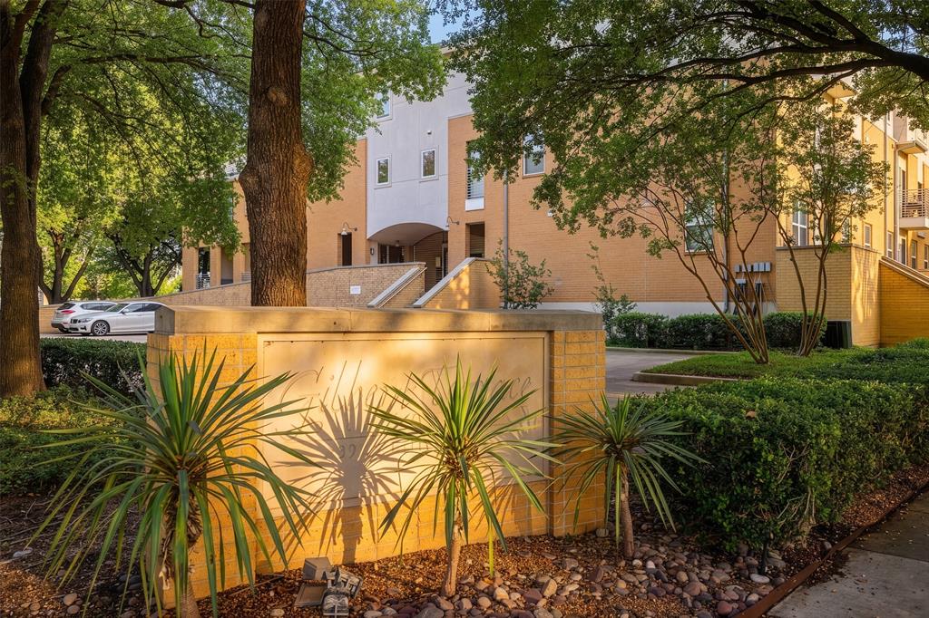 3922 Gilbert Avenue, Unit 214 Dallas, TX 75219 - Photo 22 of 27 Multi-story building exterior featuring brick and stucco finishes, mature trees, manicured shrubs, and a landscaped entrance with a stone-clad retaining wall