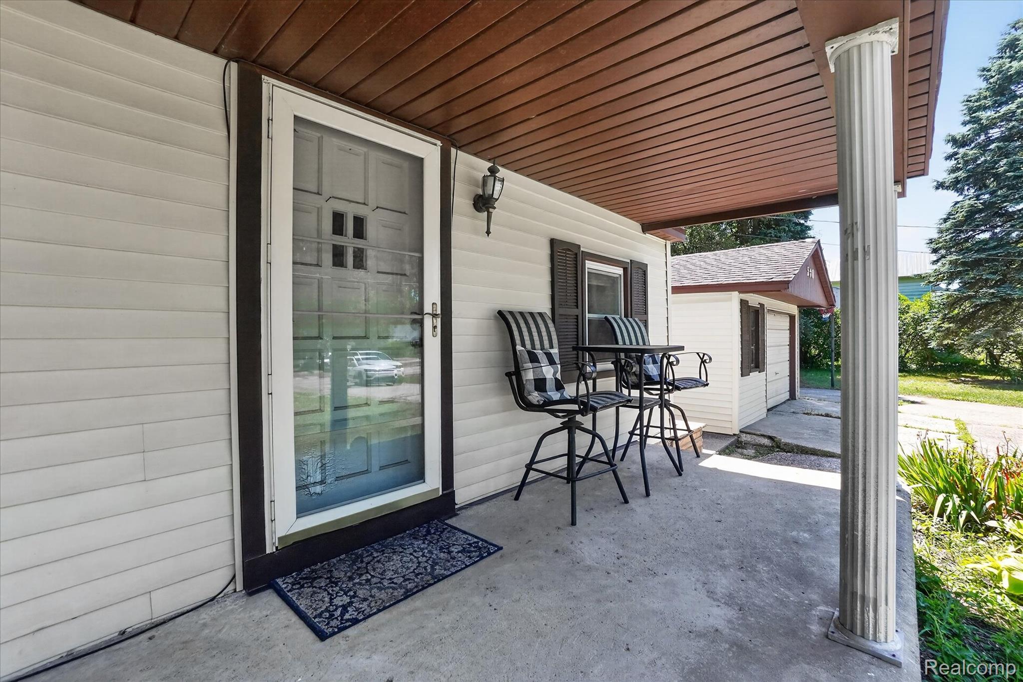 508 Deland Road Flushing, MI 48433 - Photo 6 of 38 Covered concrete porch featuring a decorative column, white vinyl siding, dark shutters, and a wood-finish soffit