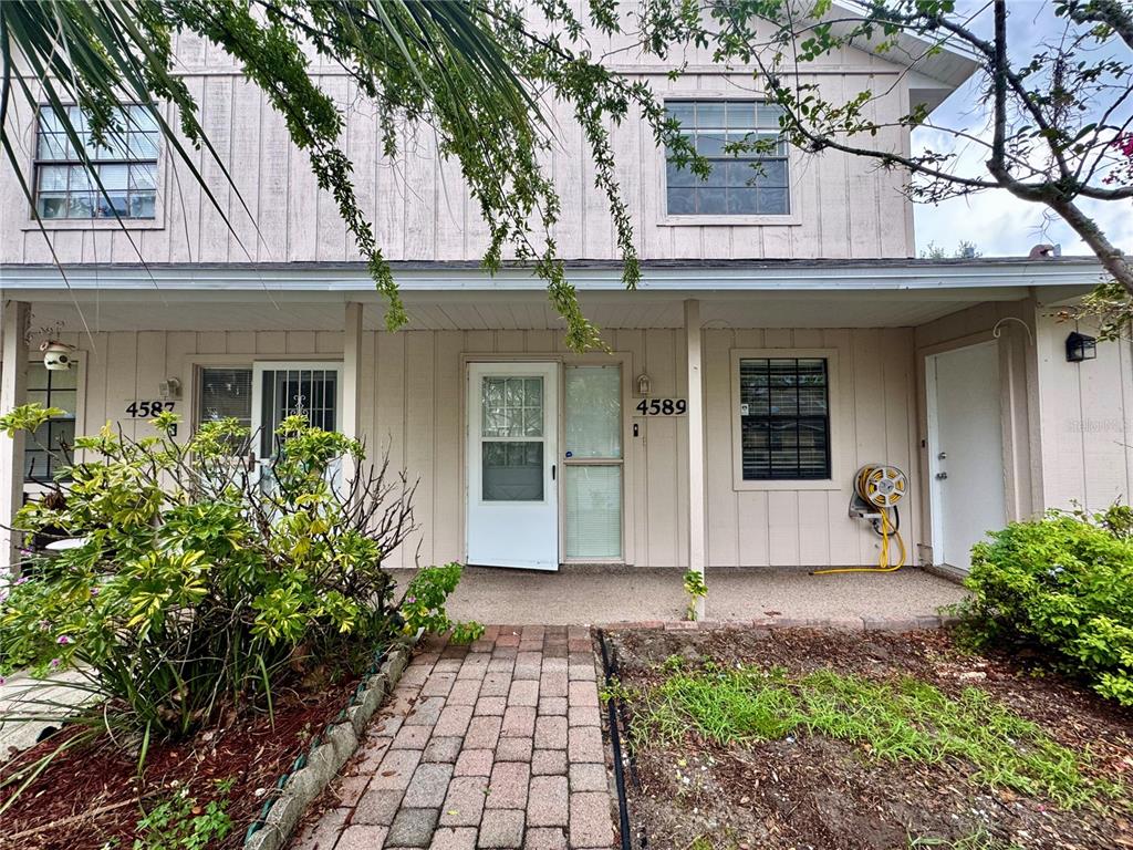 a view of a white house with large windows and a large tree with flower plants in front of main door