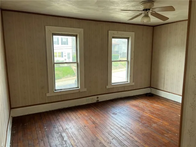 an empty room with wooden floor windows and fan