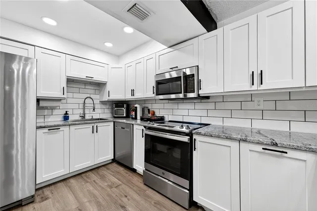 a kitchen with stainless steel appliances granite countertop a stove top oven a sink and white cabinets