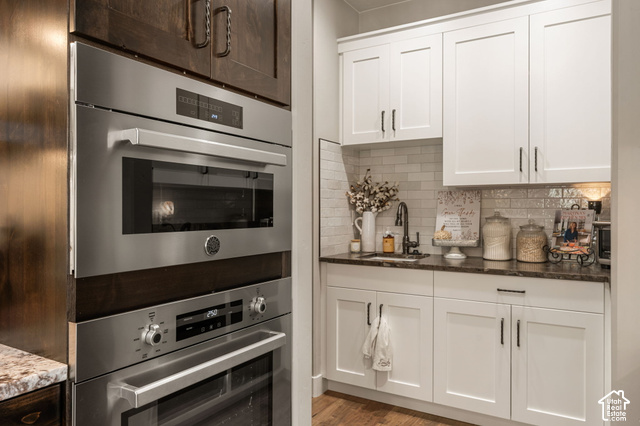 1192 East Ashdown Road Cedar City, UT 84721 - Photo 34 of 96 Built-in stainless steel double ovens, white shaker cabinetry, dark countertops, a subway tile backsplash, and a stainless steel sink with a dark faucet
