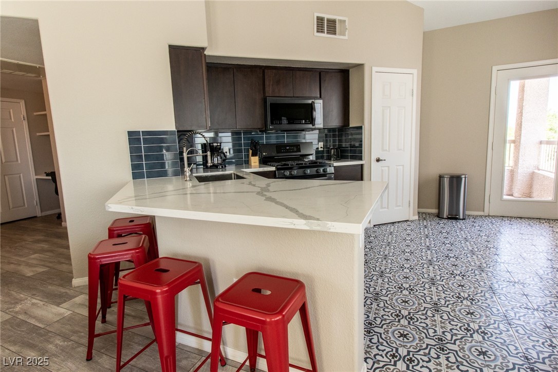 10550 West Alexander Road, Unit 2068 Las Vegas, NV 89129 - Photo 9 of 47 Kitchen featuring backsplash, a breakfast bar area, stainless steel appliances, dark brown cabinetry, and a peninsula
