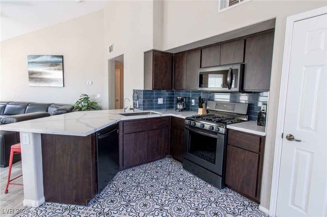 10550 West Alexander Road, Unit 2068 Las Vegas, NV 89129 - Photo 47 of 47 Kitchen with dark brown cabinets, appliances with stainless steel finishes, open floor plan, a peninsula, and decorative backsplash